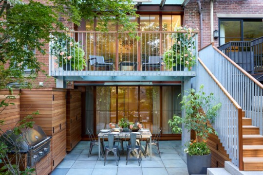 Two-level patio with an upper balcony seating area, a lower six-seat dining table, grill, planters, privacy screens, and a staircase.