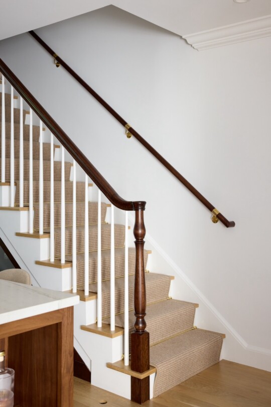 Interior staircase with carpeted treads, white balusters, a dark wood handrail, brass accents, and a carved newel post at the base.